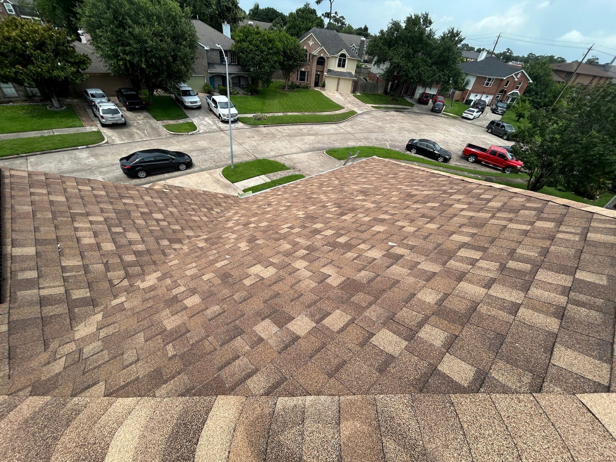 Finished tan architectural shingle roof viewed from the ridge, looking down over a suburban street