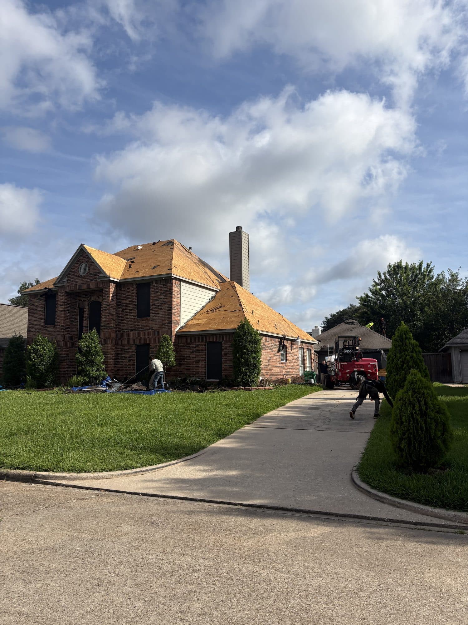Two-storey brick home mid roof replacement, decking exposed and the crew working from the driveway